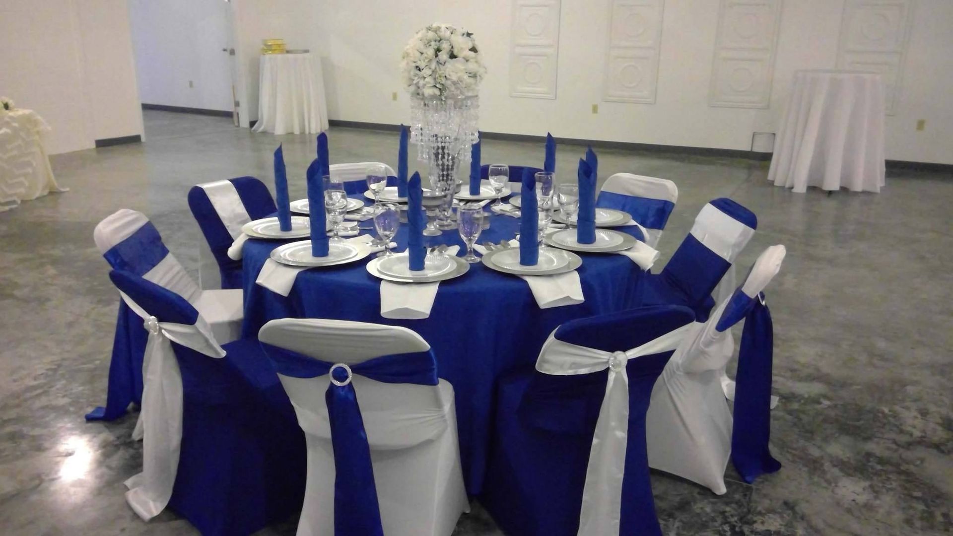 Round banquet table with blue-and-white chair covers in a white event hall