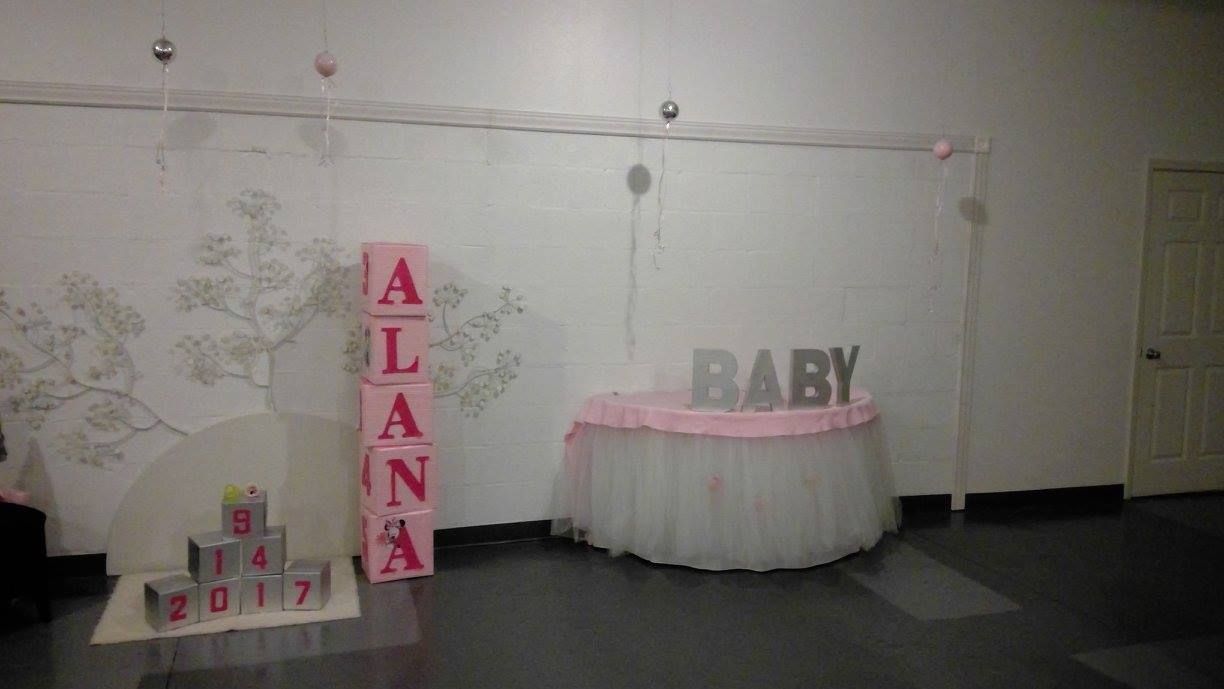 Baby shower table with pink skirt, “BABY” letters, and a vertical “ALANA” sign against a white wall