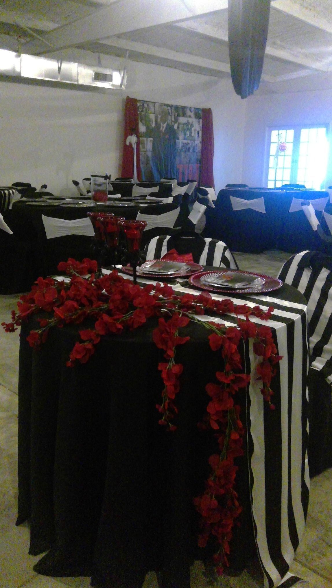 Decorated indoor event room with black-and-white striped tables, red floral centerpieces, and chairs set up for guests