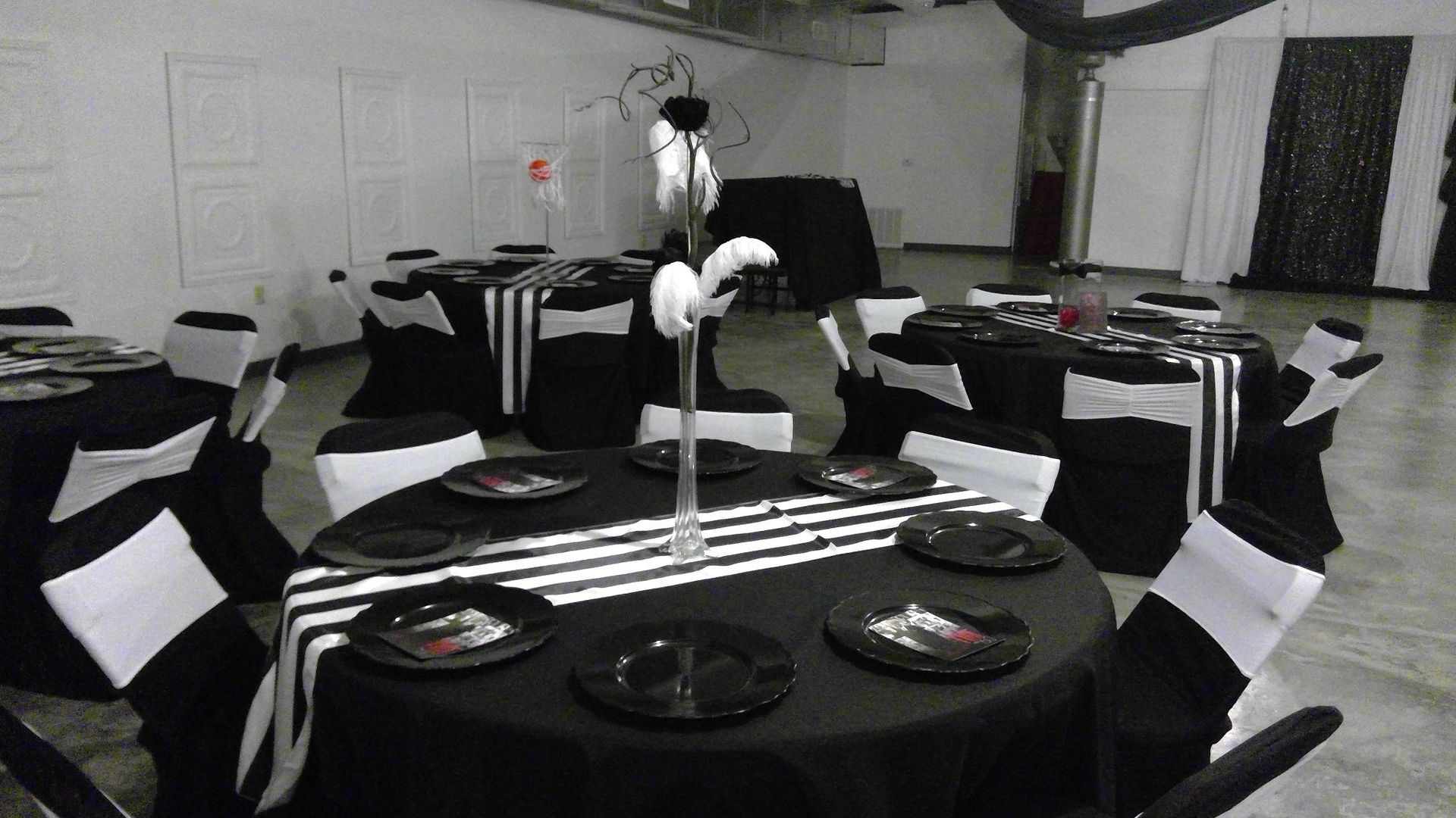 Black-and-white banquet hall with round tables, black tablecloths, and folded white napkins on chairs.