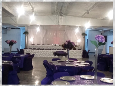 Banquet hall with purple table settings, floral centerpieces, and a decorated stage at the back
