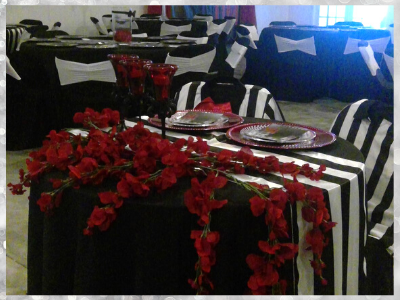 Banquet tables with black-and-white striped linens and red floral centerpieces in a decorated event room