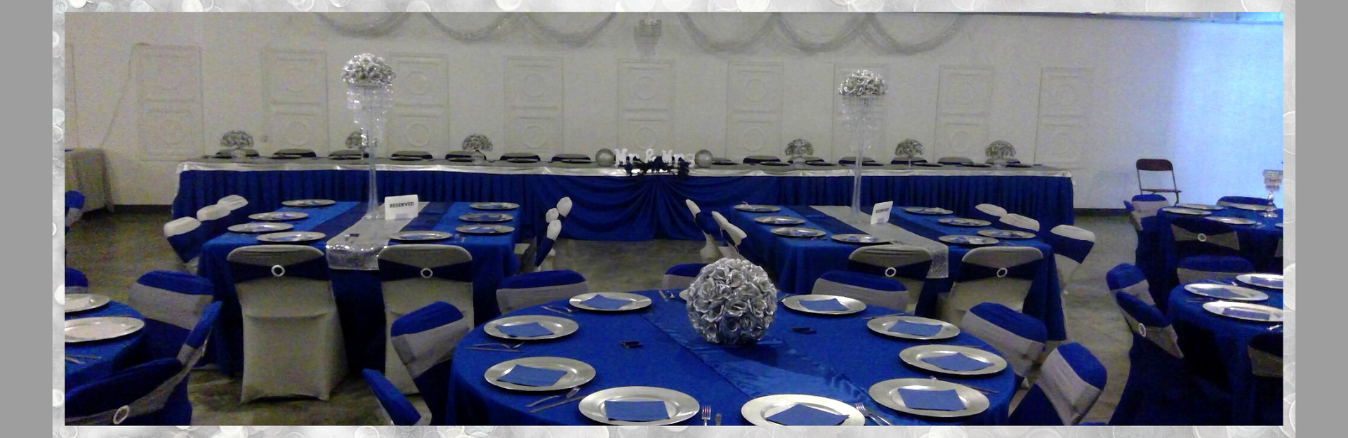 Blue-and-white banquet hall set for a formal event, with round tables and neatly arranged plates and chairs.