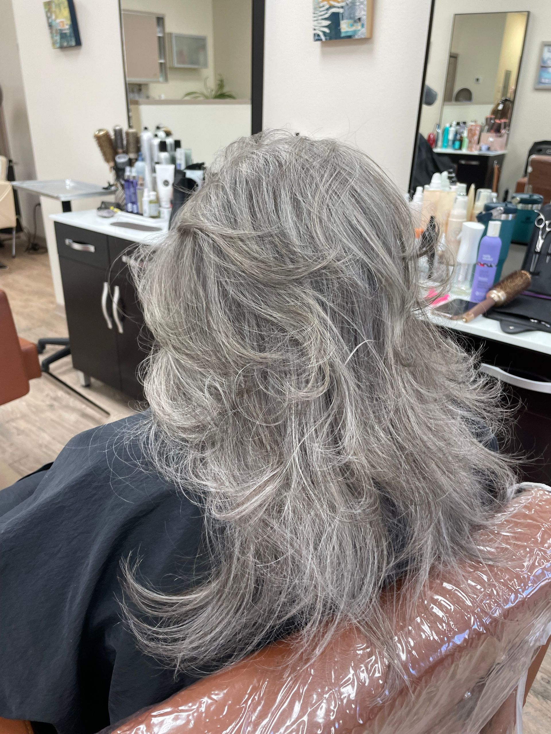 A woman with gray hair is sitting in a chair in a salon.