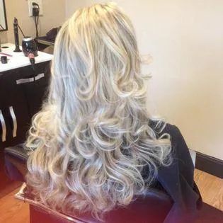 A woman with long blonde hir is sitting in a chair in a salon.