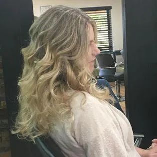 A woman with long blonde hair is sitting in a chair in a salon