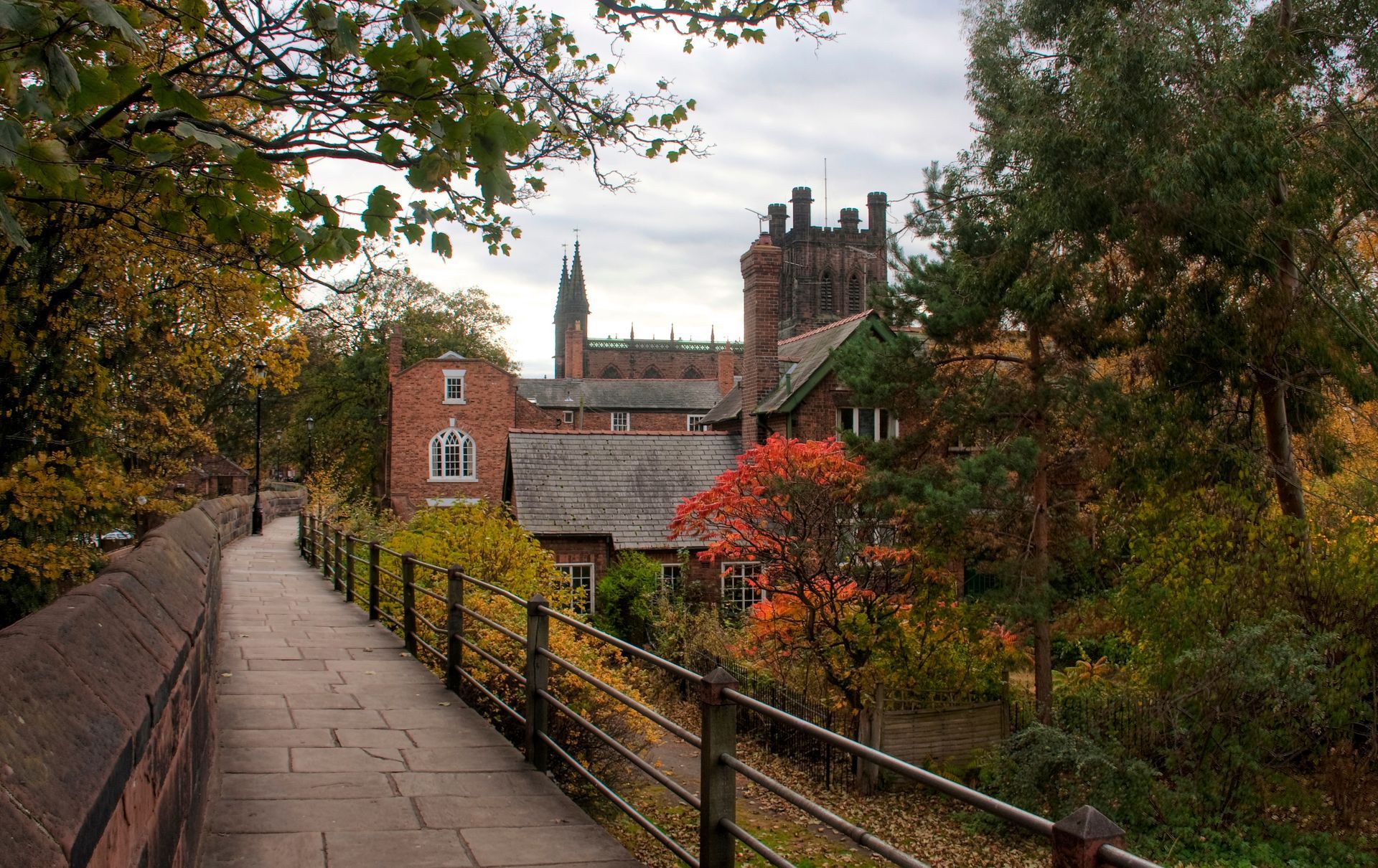 Tree-lined path on the Roman Walls, Chester leading to a historic brick building with Cathedral towers in an autumn landscape