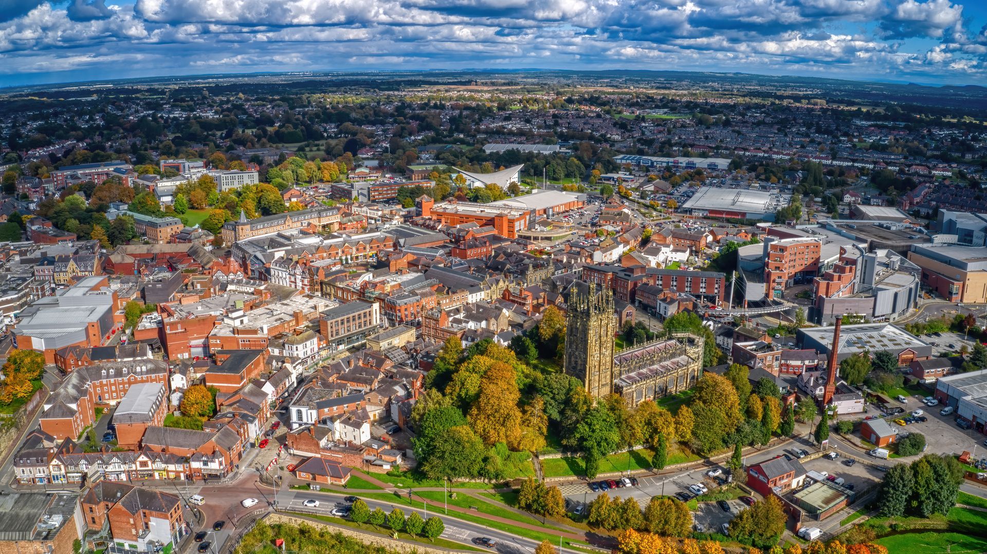 Aerial view of a historic city center of Chester with red-roofed buildings, a cathedral, and a cloudy sky.