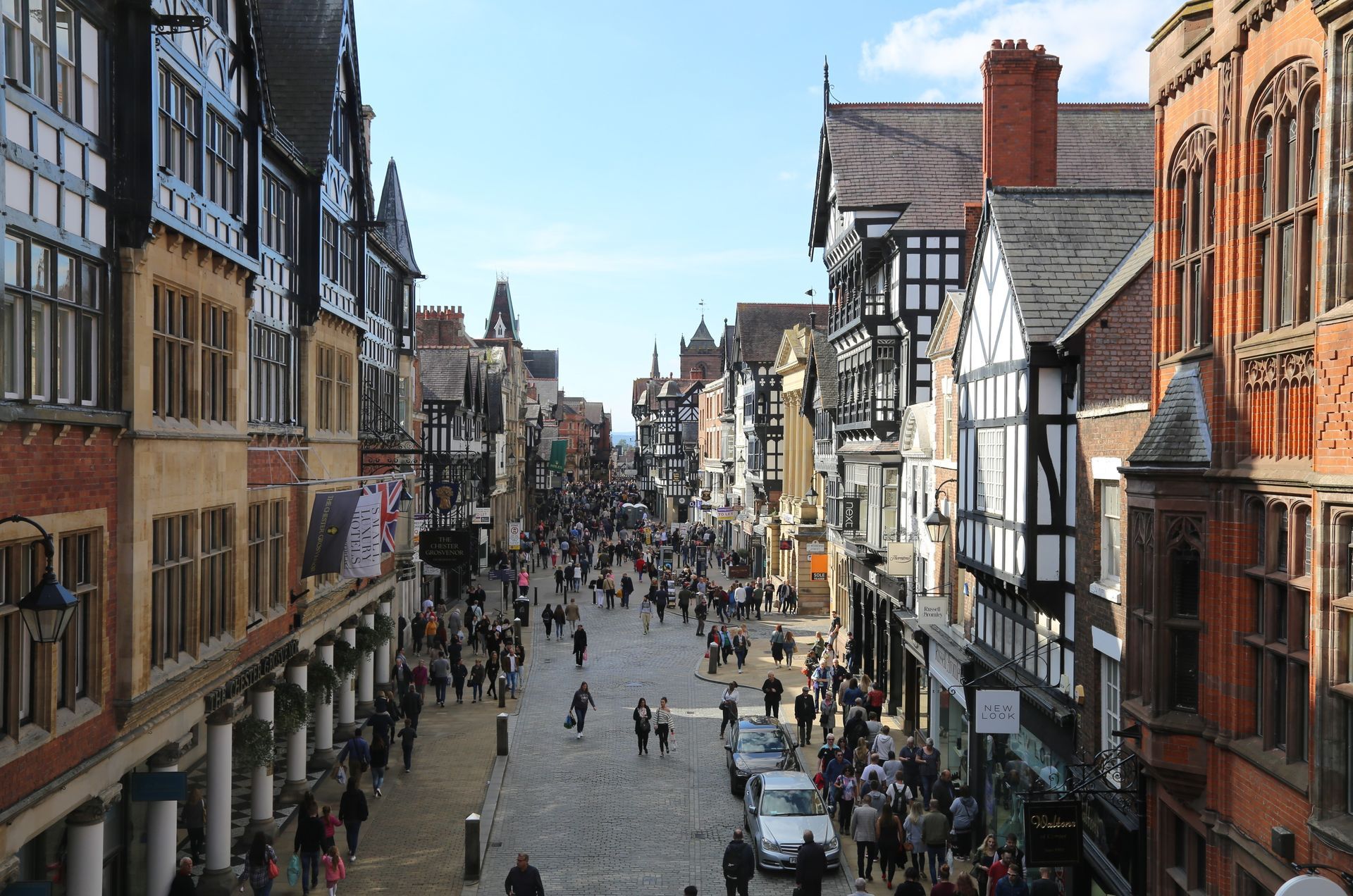 Crowded historic shopping street in Chester, Cheshire with timber-framed buildings under a blue sky