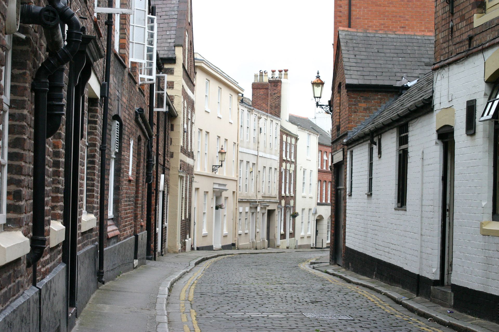 Narrow cobblestone street in Chester lined with old brick and white houses in a quiet town.