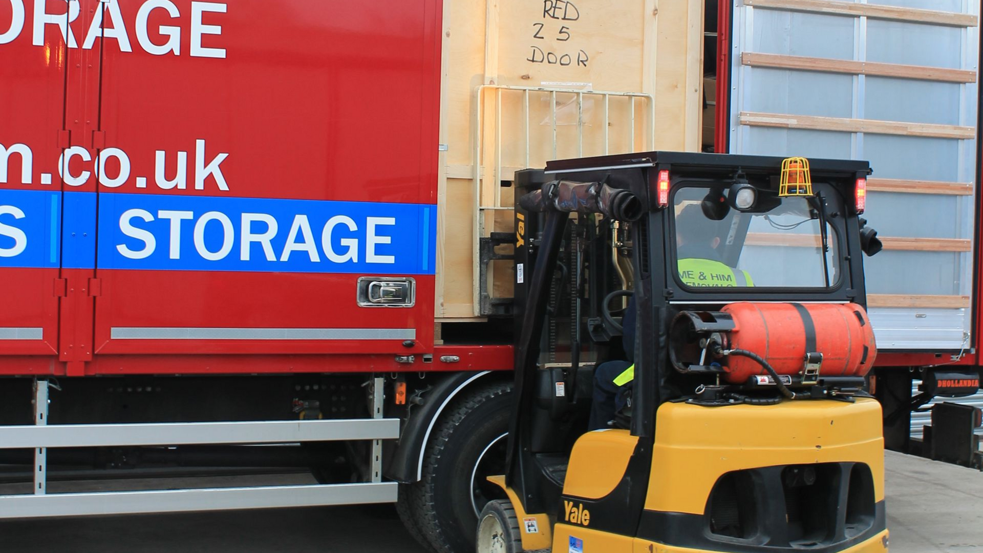 Yellow forklift unloading a red Me & Him Removals & Storage truck with blue branding inside a warehouse area
