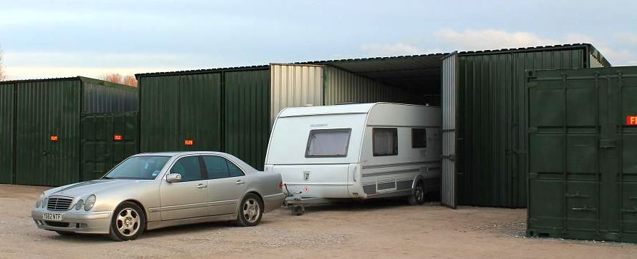 Blue SUV towing a white caravan from a green secure storage unit onto a paved lot