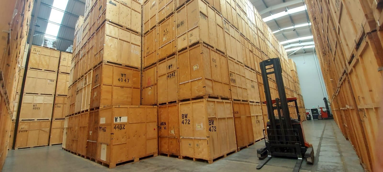 Yellow Yale forklift in a Me & Him Removals & Storage warehouse aisle between stacked wooden crates.