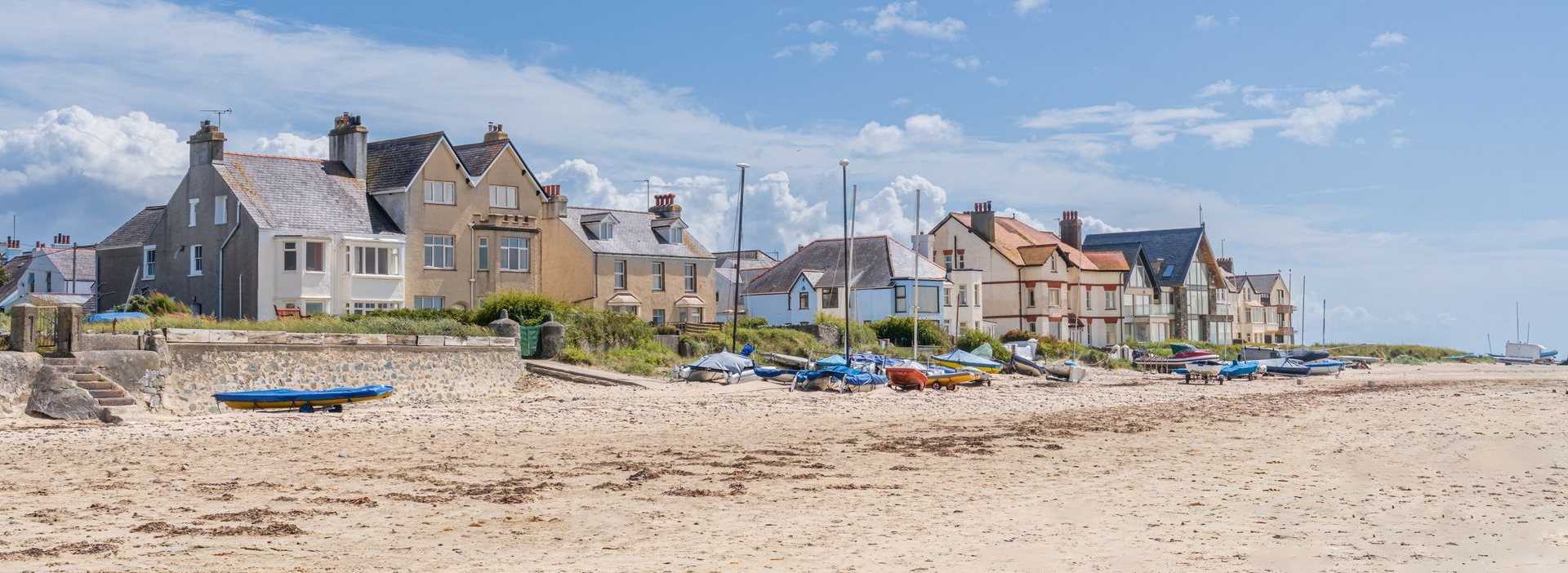 Sandy beach at Rhosneigr, Anglesey with colourful houses and a blue sky along the shoreline.