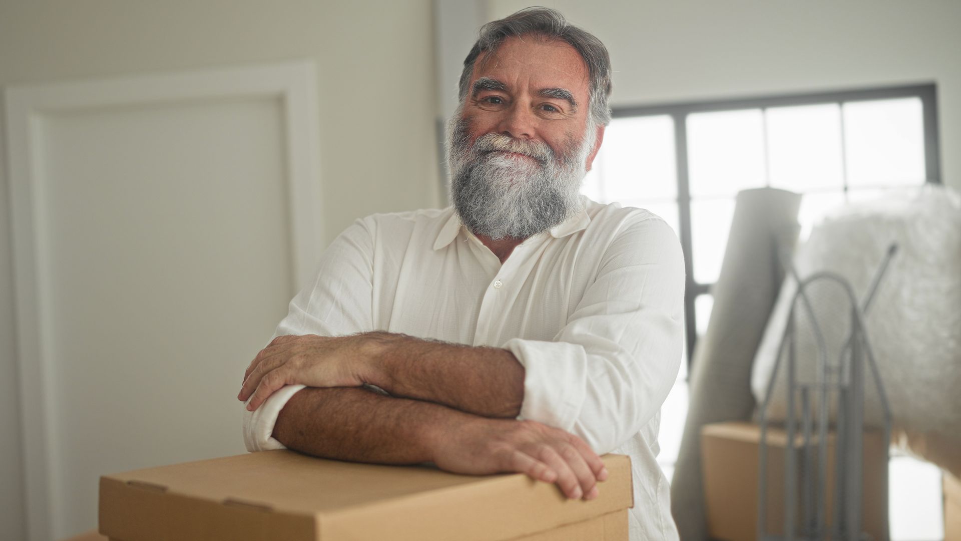 Smiling Me & Him Removals & Storage customer leaning on moving boxes in a bright room.