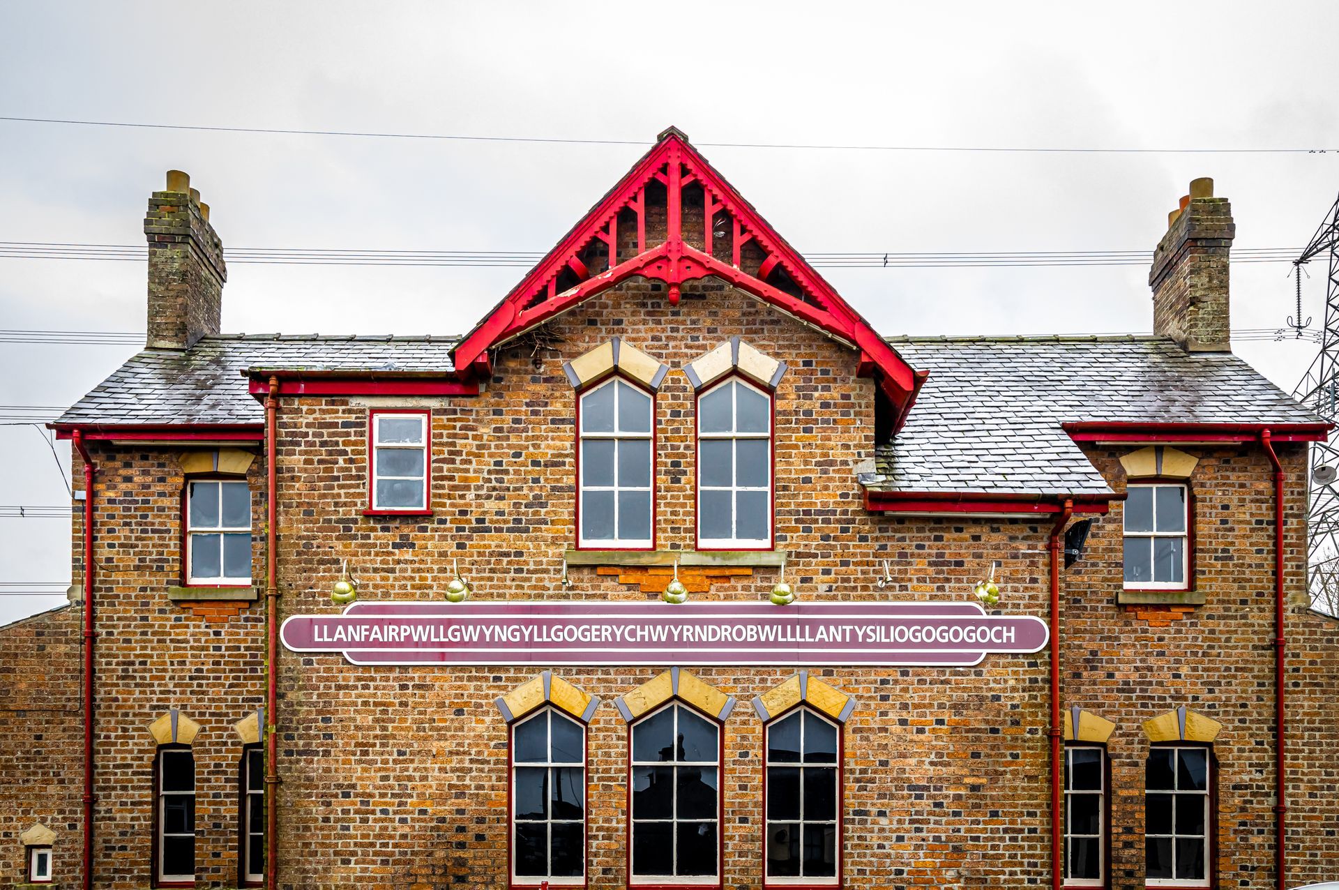 Brick railway station at Llanfairpwllgwyngyllgogerychwyrndrobwllllantysiliogogogoch with red gabled roof and banner sign