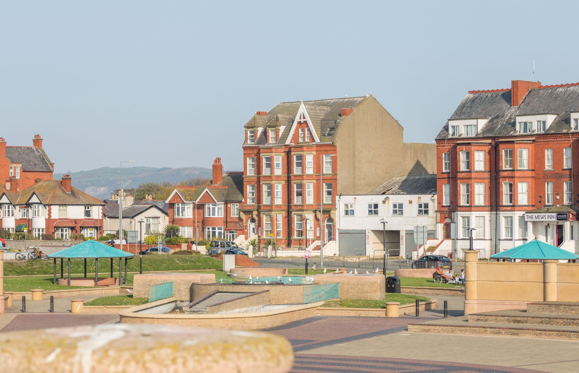 Seaside town of Rhyl with square red-brick buildings, sandy paths, and benches under a clear sky