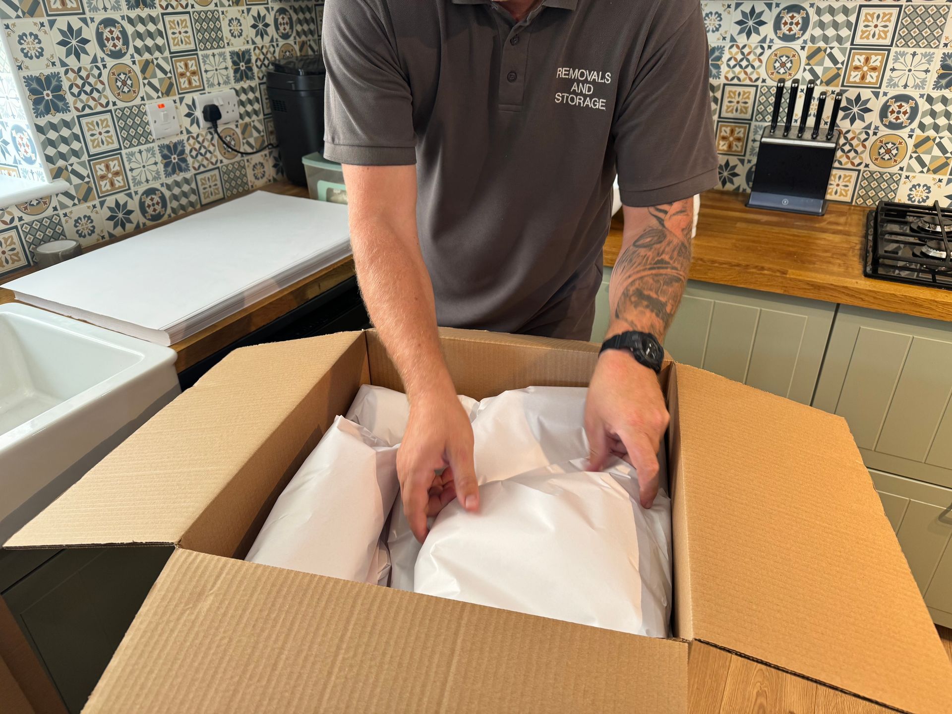 Two Me & Him Removals & Storage movers in maroon shirts sealing a cardboard box with packing tape
