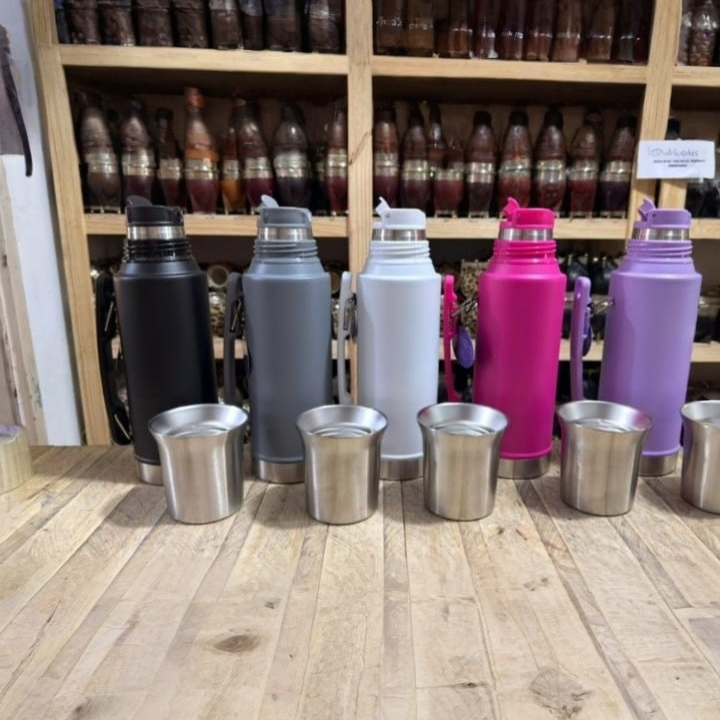 Cinco termos de colores y cinco tazas de acero inoxidable expuestos en un estante de madera en una tienda.