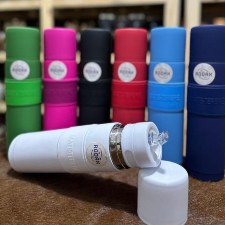 Seis botellas térmicas de colores alineadas detrás de una botella blanca sin tapón sobre una mesa de madera.