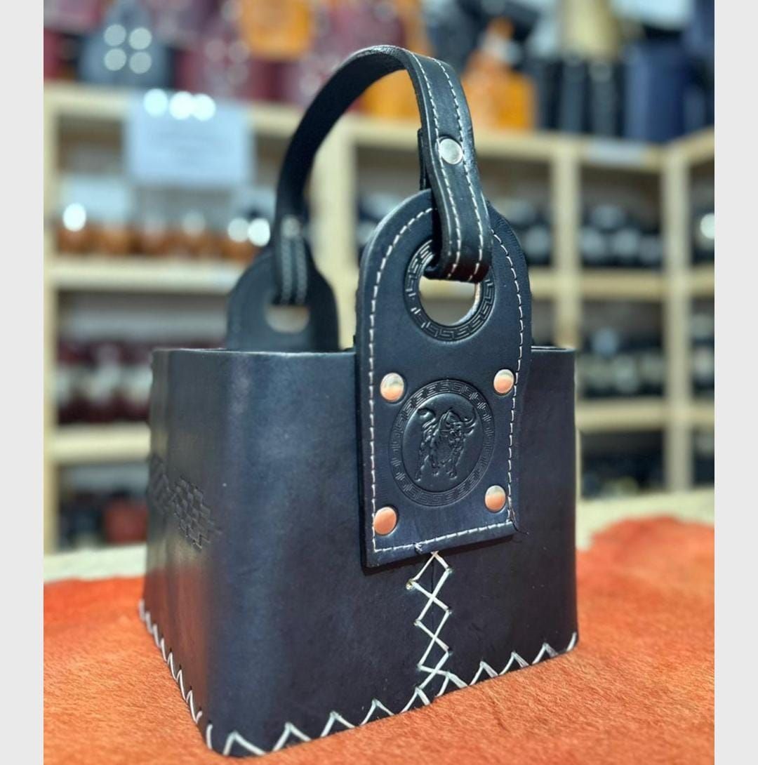 Bolso de mano de piel negra con ribete cosido y asas de lazo sobre una superficie naranja.