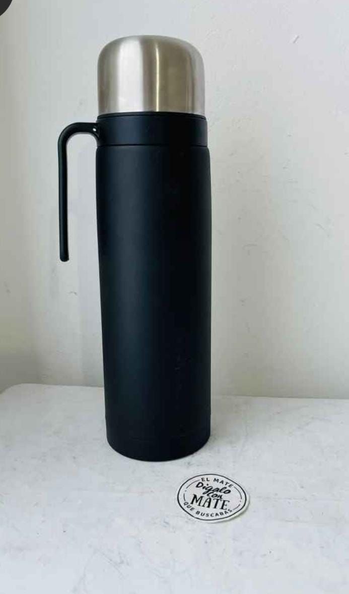 Botella termo negra con tapa y asa plateadas sobre una superficie blanca.