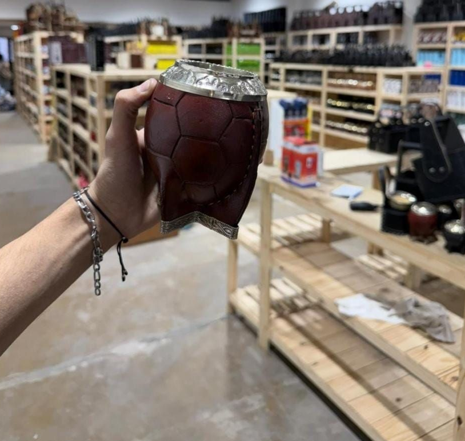 Una mano sostiene una calabaza mate de color granate oscuro en el pasillo de una tienda con estantes al fondo.