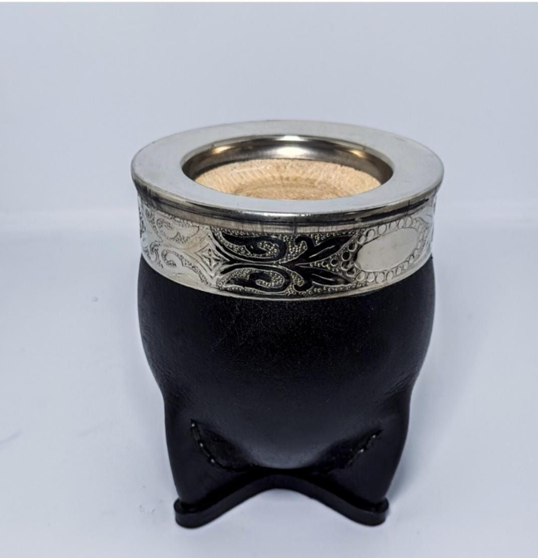 Taza de mate negra y plateada con borde decorativo de metal sobre fondo claro.