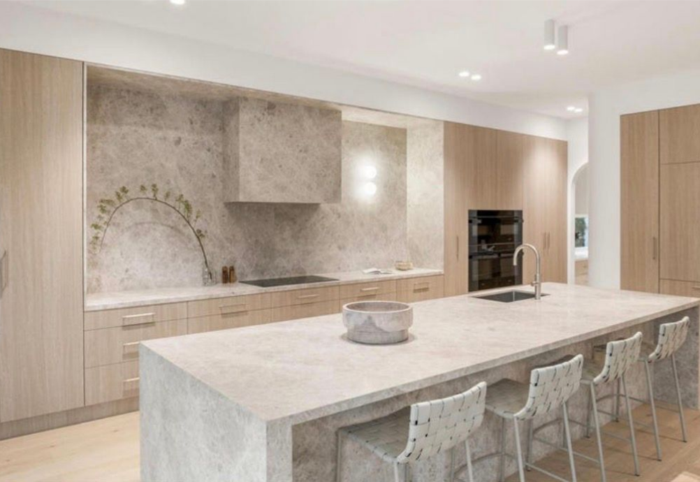 A modern kitchen featuring light wood cabinetry, stone countertops, a matching stone backsplash, and a central island.