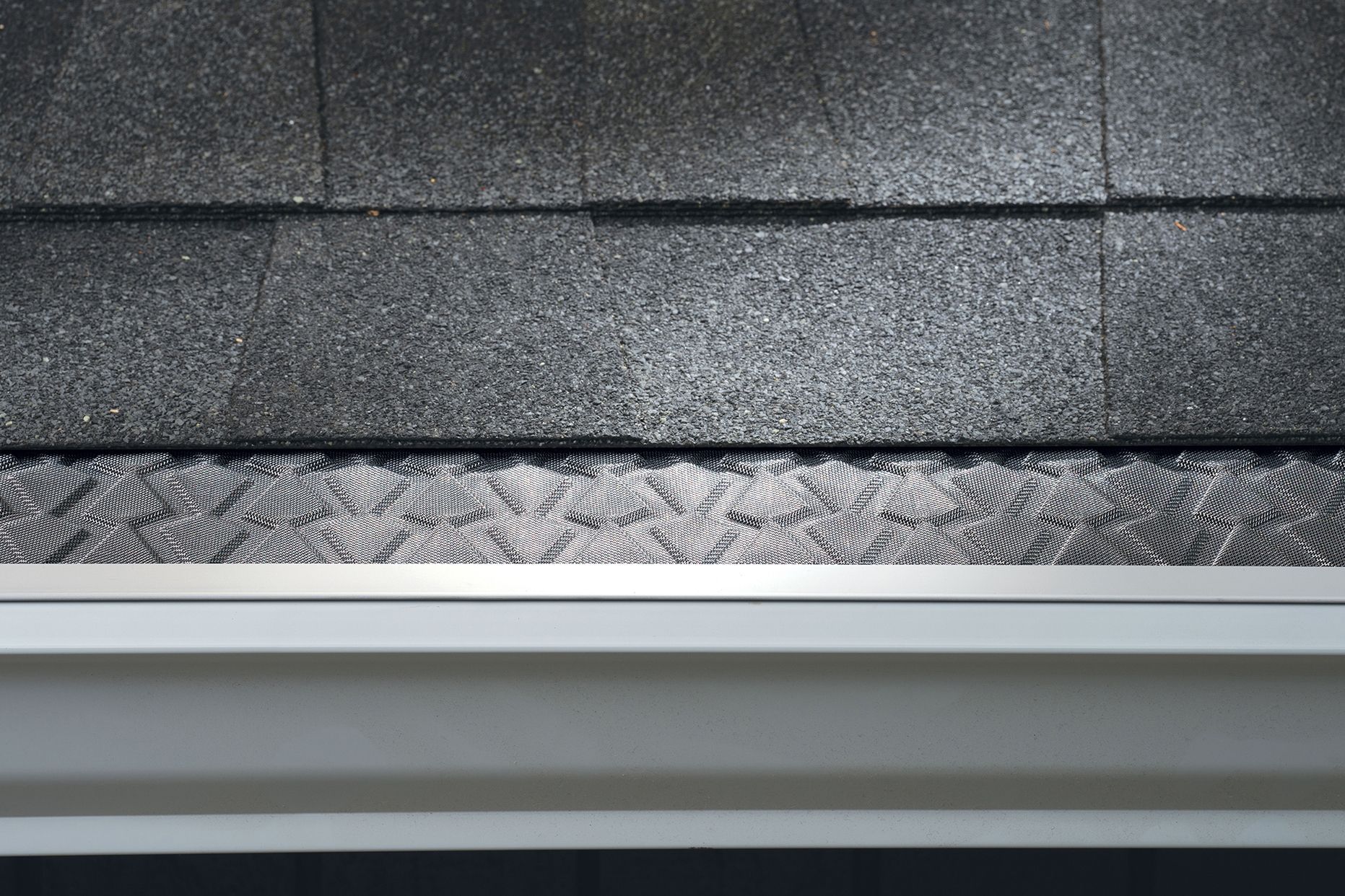 Leaf Defender stainless-steel raised-pattern gutter guard with aluminum rails installed beside roof shingles