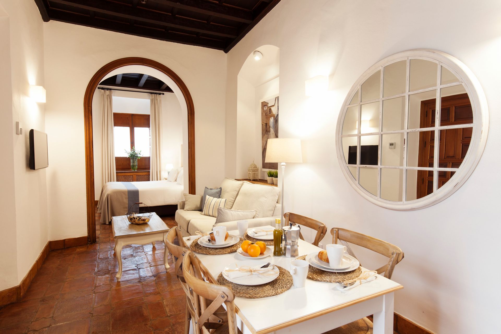 Bright dining room with white table, wooden chairs, round mirror, and arched doorway to a sitting area