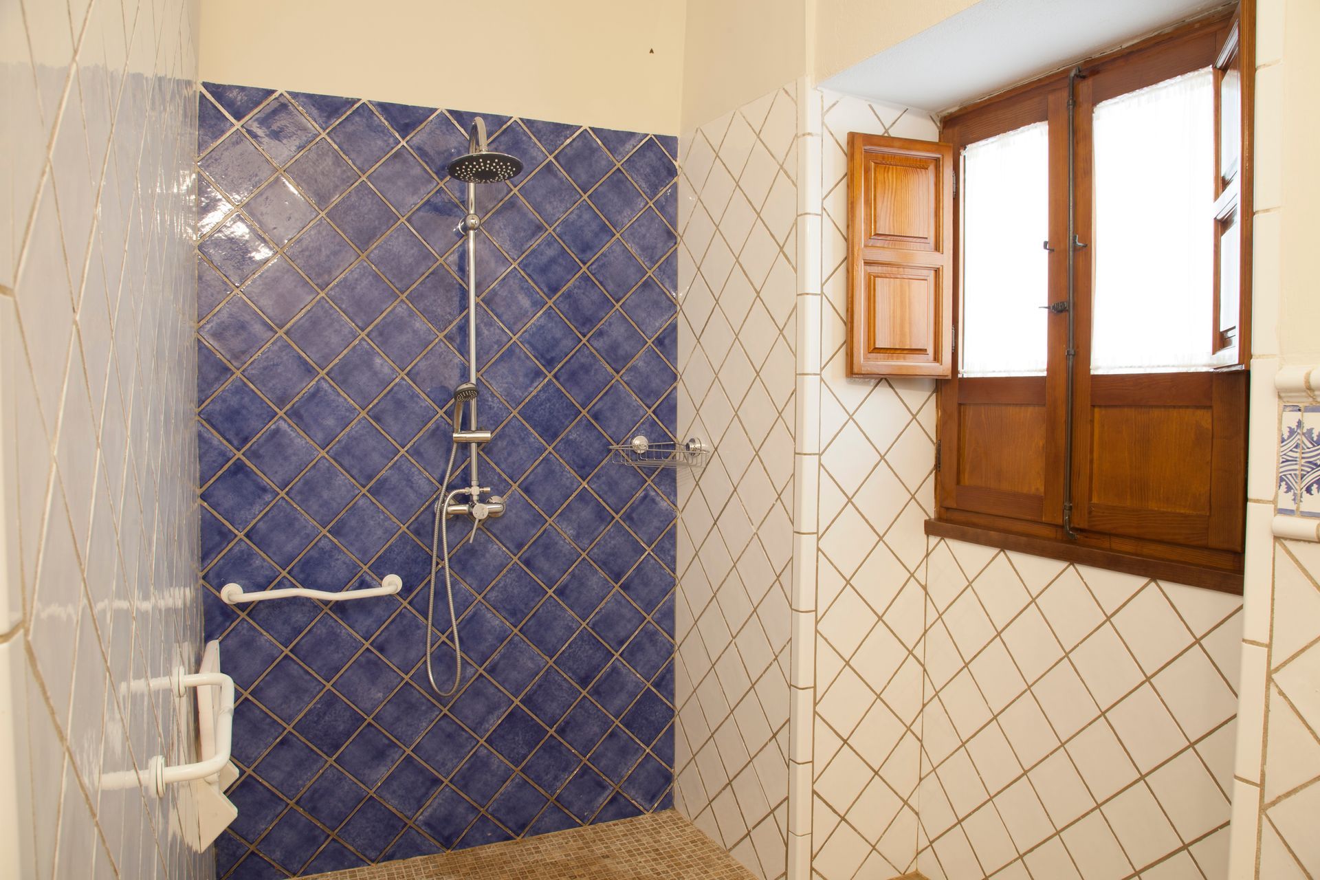 Bathroom with blue tiled shower, white walls, and a wooden-framed window with shutters