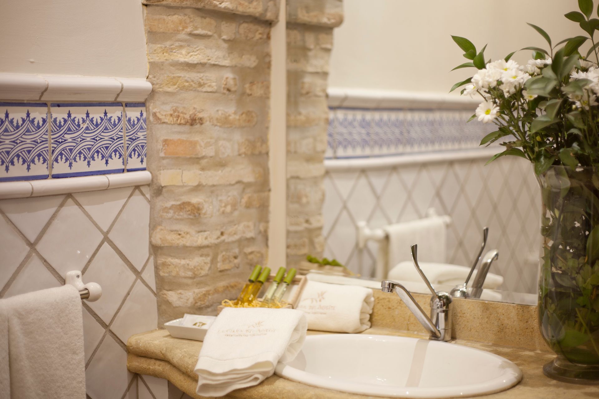 Bathroom sink with stone accent wall, patterned tile border, folded towels, and a potted plant.