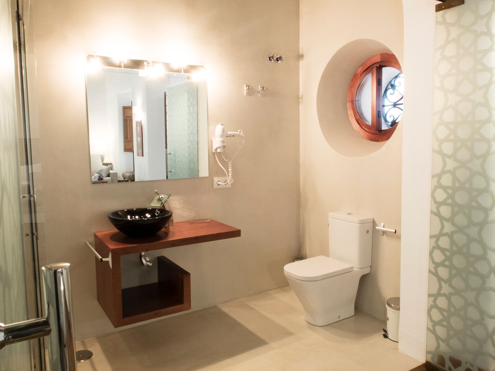 Modern bathroom with glass shower, sink vanity, toilet, and round window.