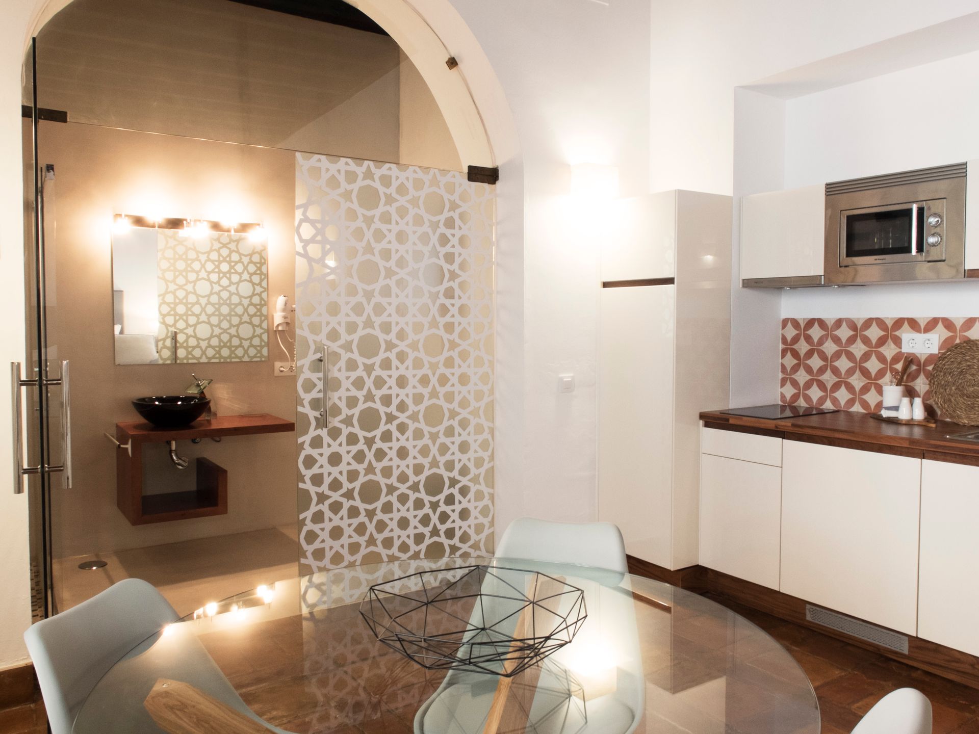 Modern kitchen and dining area with white cabinets, patterned backsplash, and glass table under an arched doorway