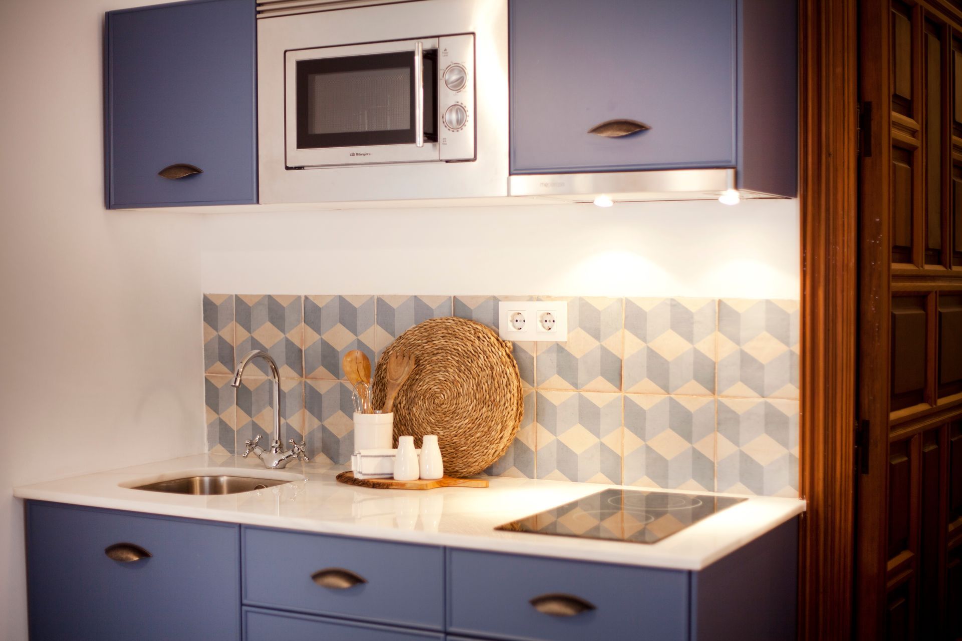 Compact kitchen nook with blue cabinets, white countertop, tile backsplash, and built-in microwave.