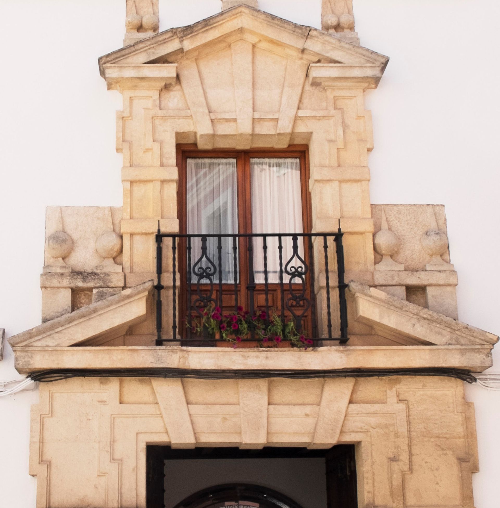 Stone balcony with wrought-iron railing and French doors on a beige building facade