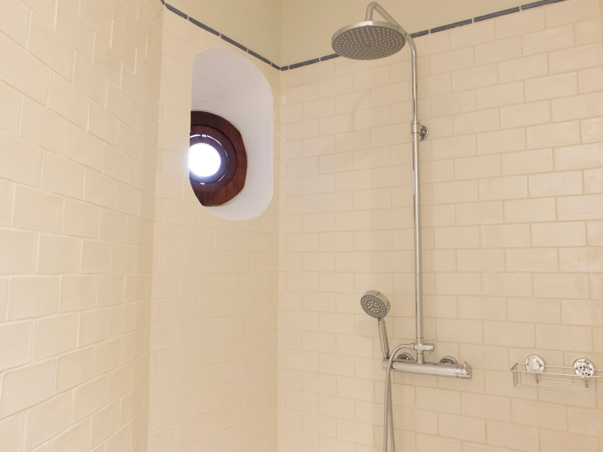 White-tiled shower with a handheld showerhead and circular window.