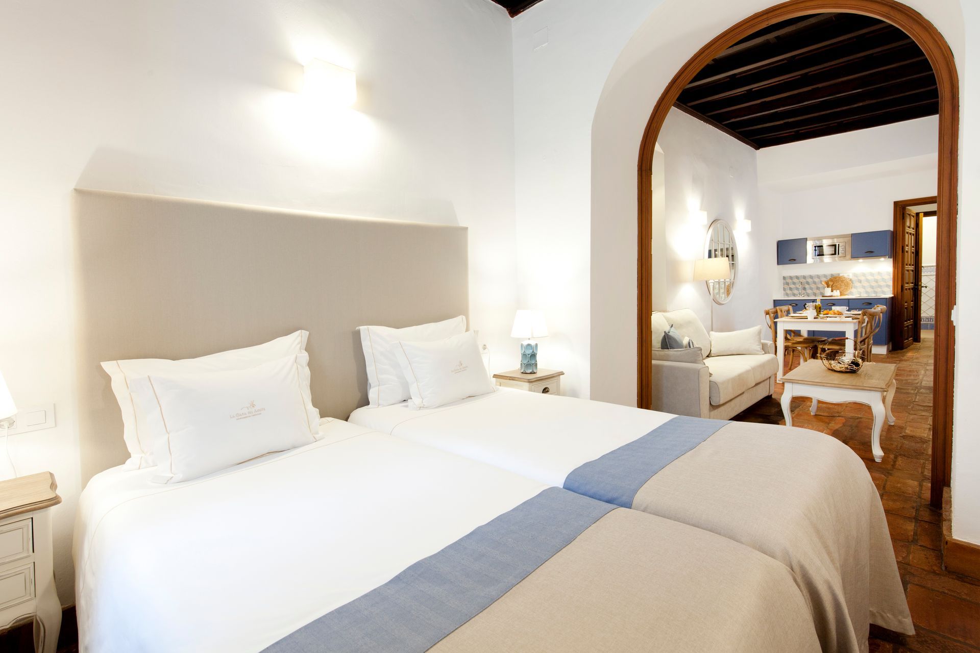 Bright white hotel bedroom with a large bed, archway, and sitting area beyond