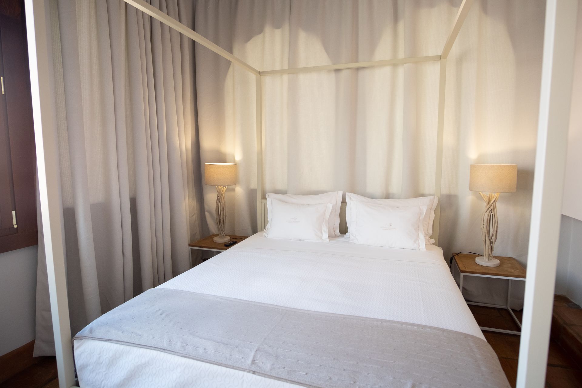 White canopy bed with two pillows and bedside lamps in a softly lit bedroom