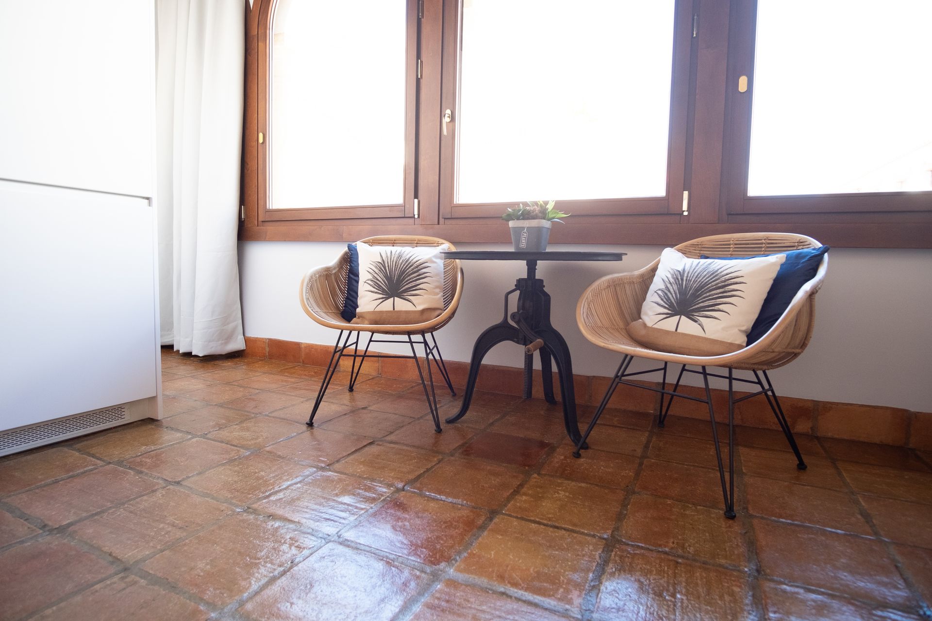 Two beige chairs beside a small black table in a bright room with wooden floor and large windows