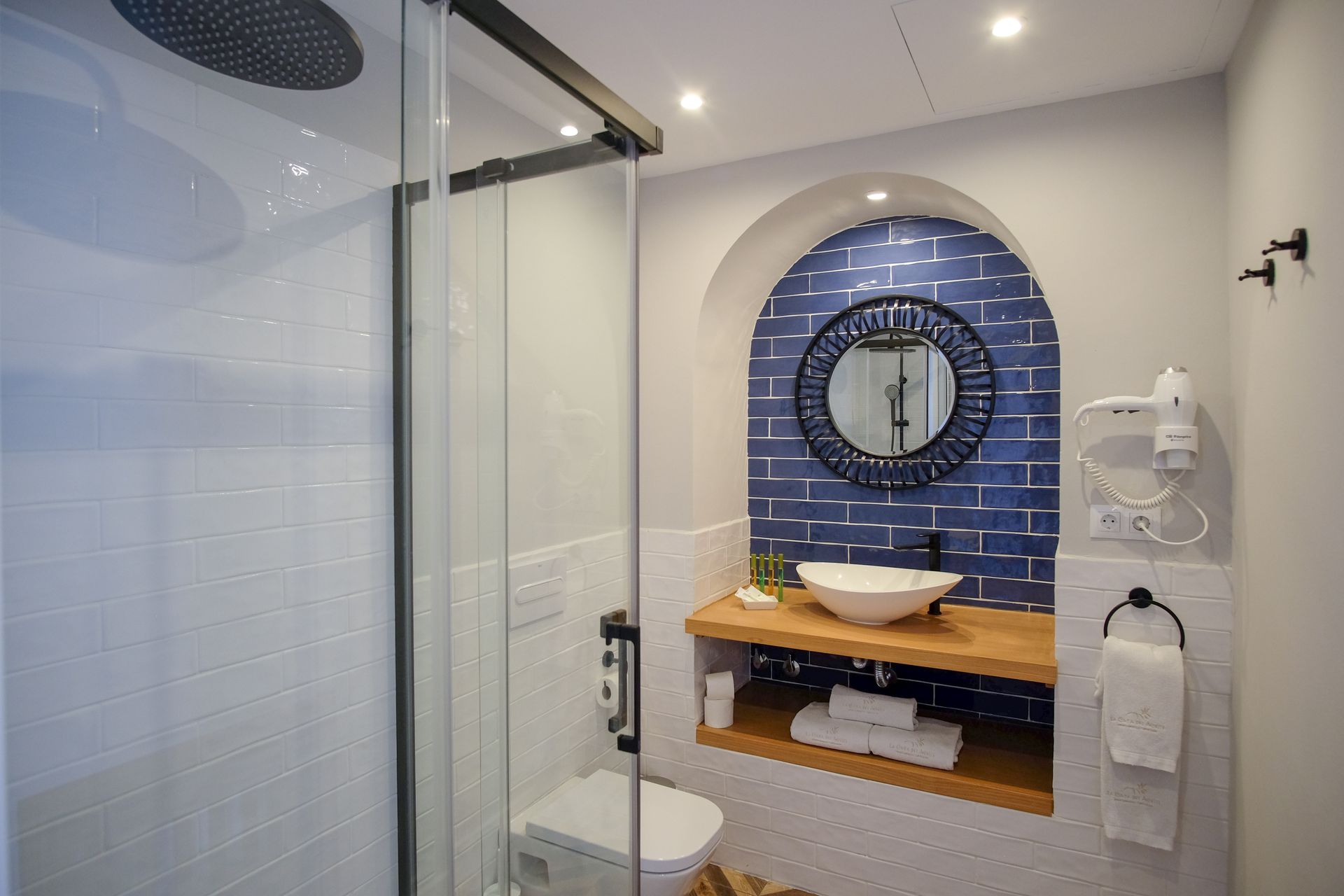 Modern bathroom shower and sink vanity with blue tiled arch and round mirror