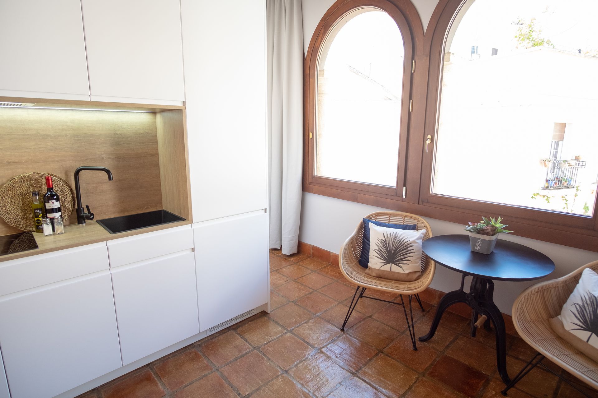 Bright kitchen nook with a small round table, wicker chairs, and a sink by a sunlit arched window.