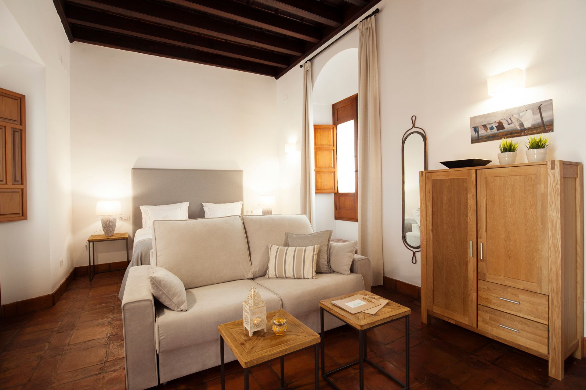 Cozy beige bedroom with wooden beams, bed, sofa, and cabinet in a bright rustic interior
