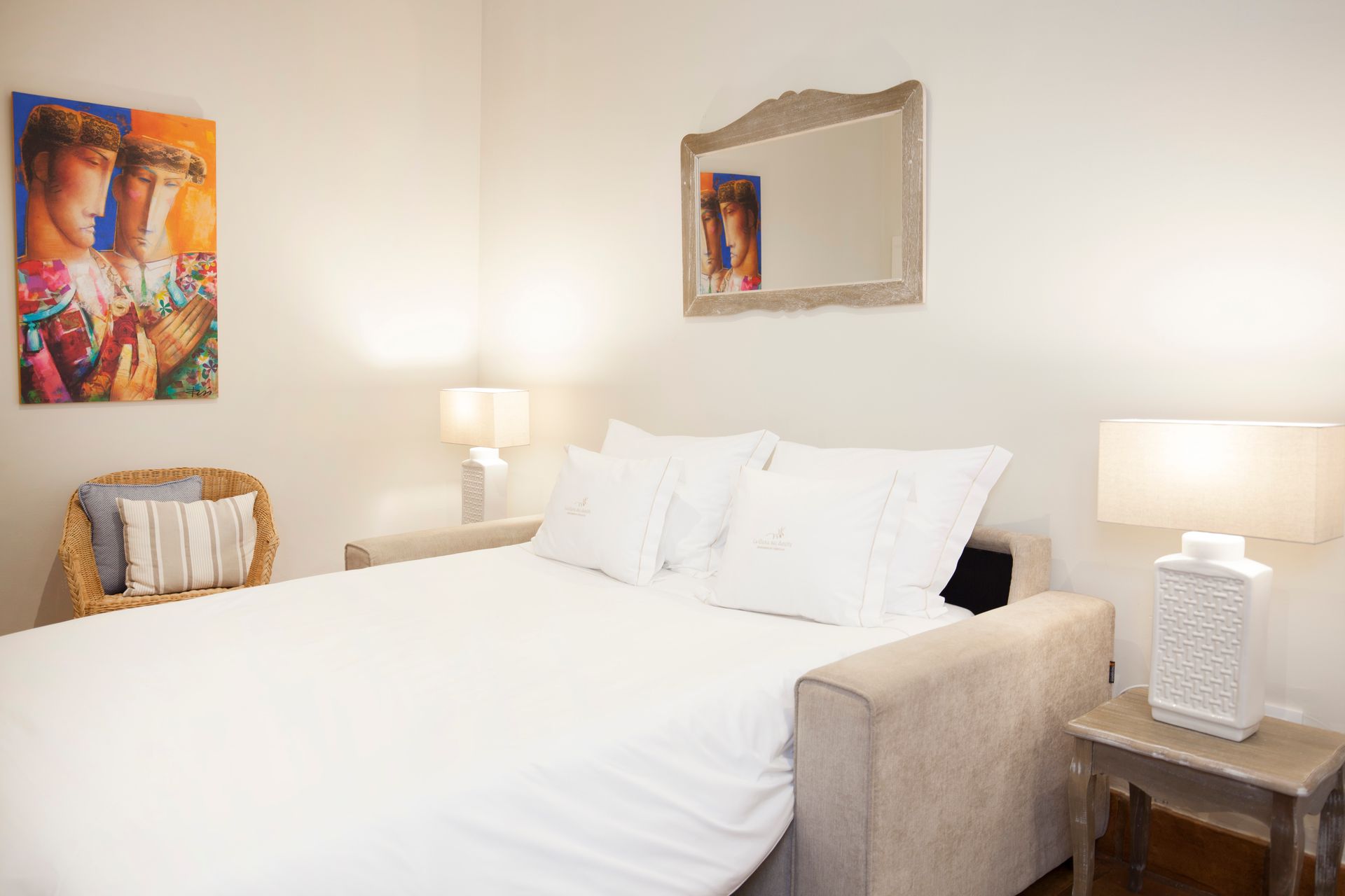 Bright bedroom with a white bed, beige furniture, lamps, and colorful wall art
