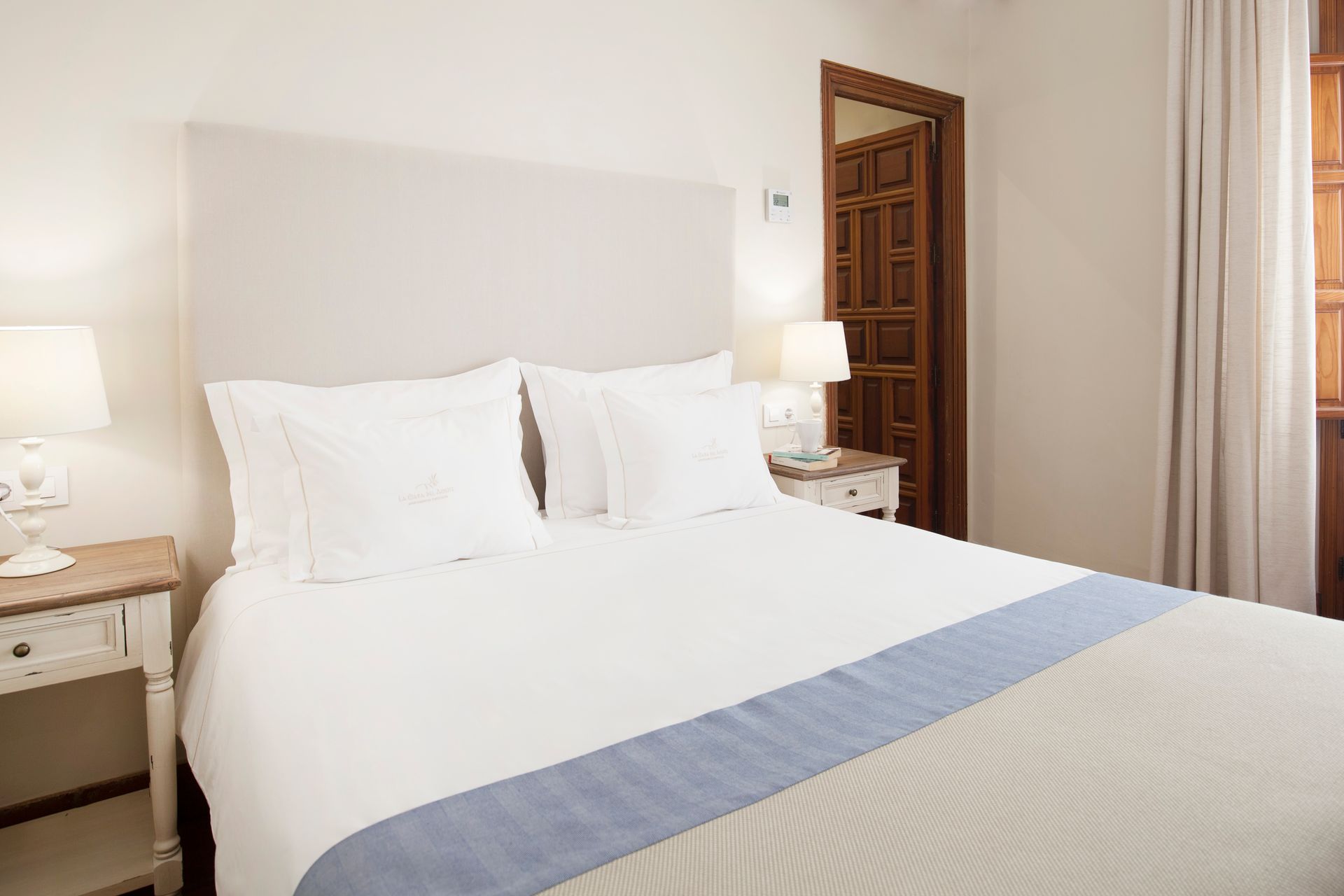 Bright bedroom with a white bed, bedside lamps, and an open wooden door