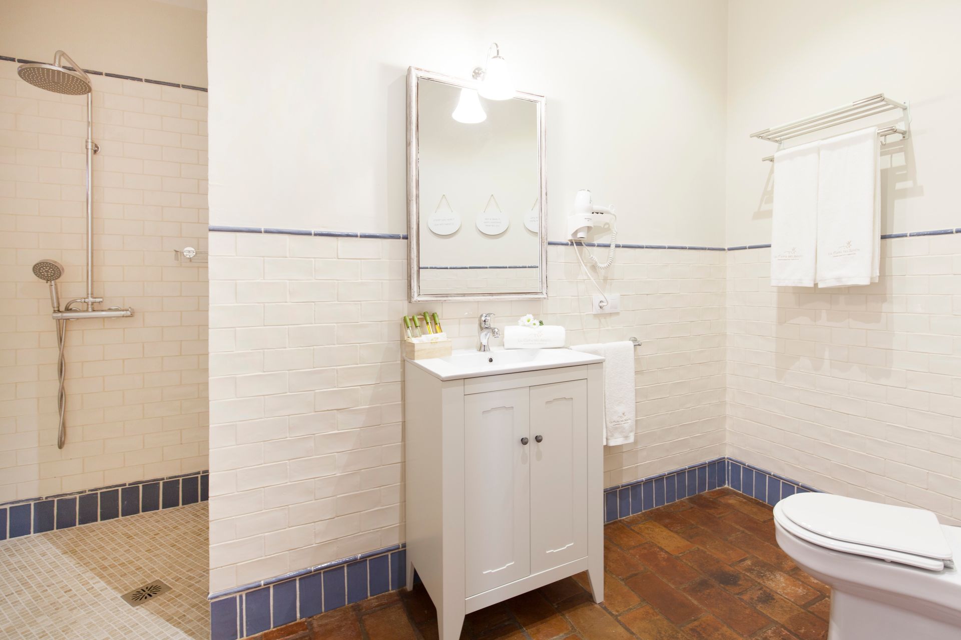 Bright white bathroom with vanity, mirror, shower, towel rack, and toilet in a tiled room.