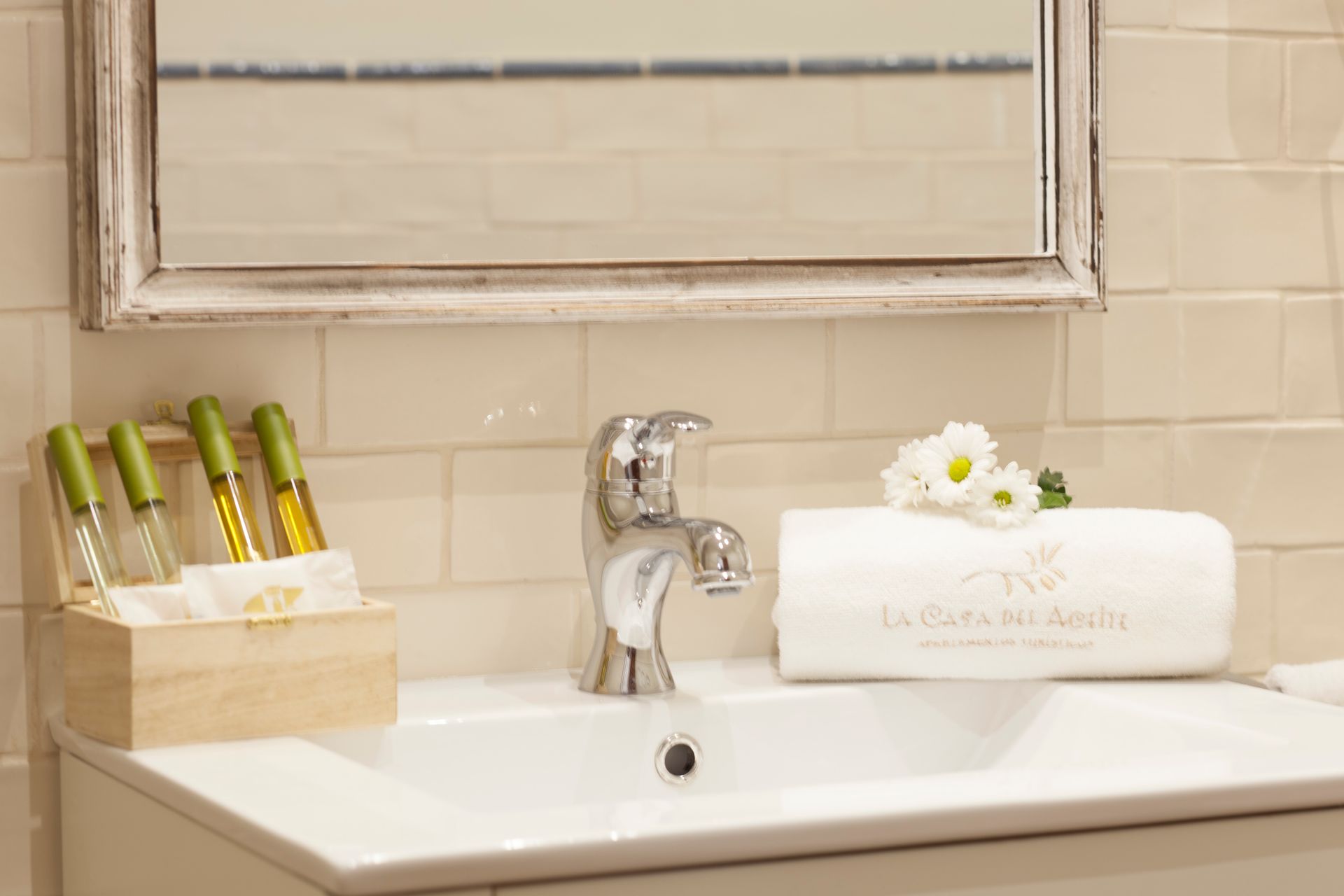 Bathroom sink with chrome faucet, soap dispenser, and a white towel with a flower on a beige counter.