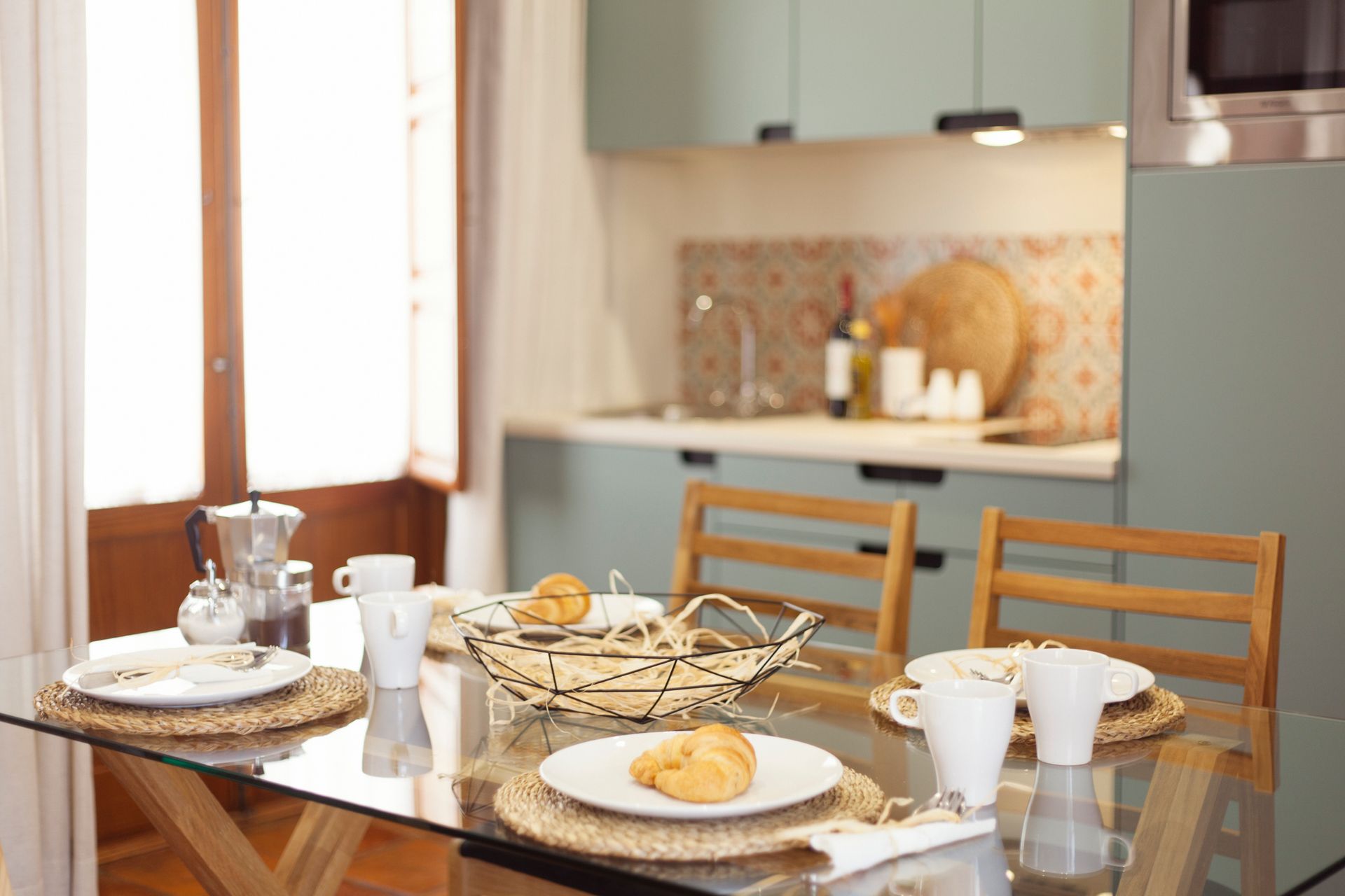 Set dining table in a bright kitchen with plates, cups, pastries, and a glass carafe