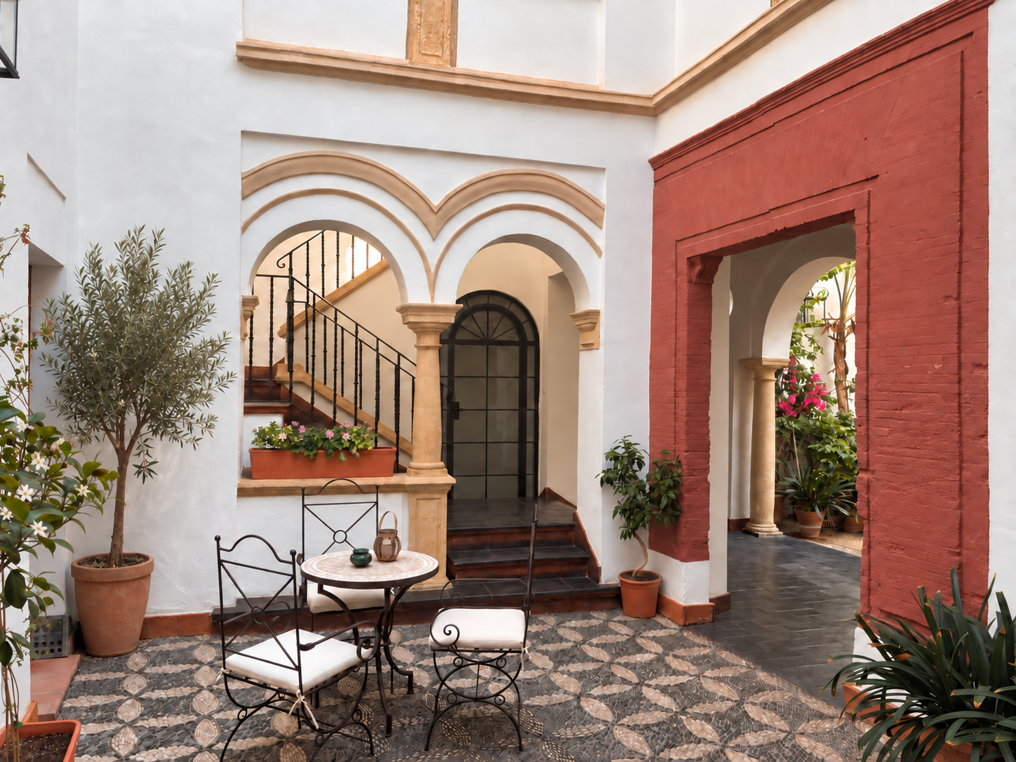 Sunlit Mediterranean courtyard with arched doorways, patterned tile floor, and outdoor seating